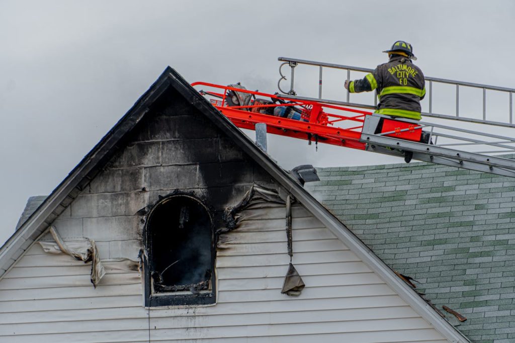 firefighter-on-building-roof-6357619 Firefighter on ladder tackling a residential roof fire in Baltimore city.