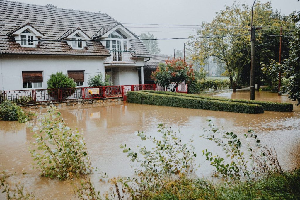 flooded-suburban-house-during-heavy-rain-28447774 A suburban house surrounded by floodwaters after heavy rain, showing impact of natural disaster.